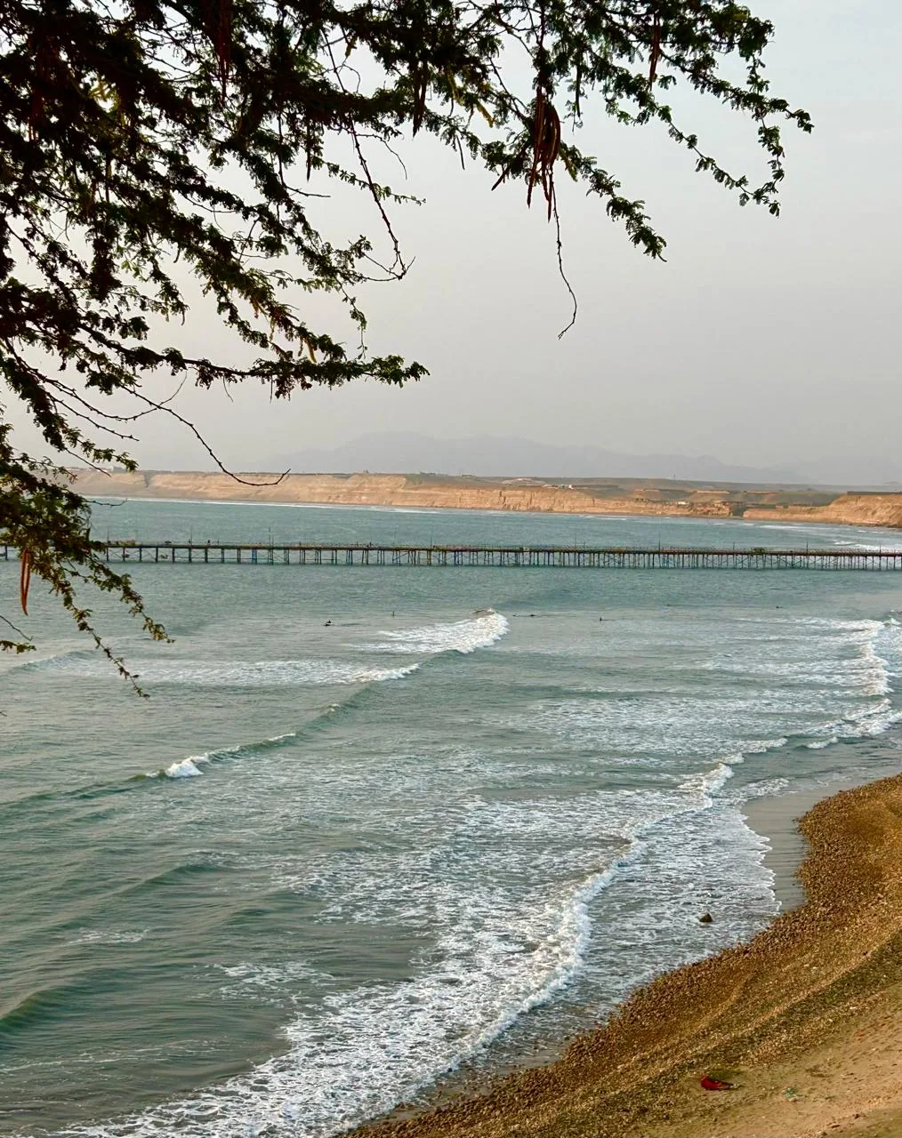 Swimmers on the town beach of Pacasmayo, with the wooden pier behind