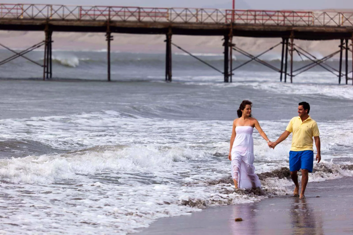 A couple walking along the shore, with the wooden pier behind