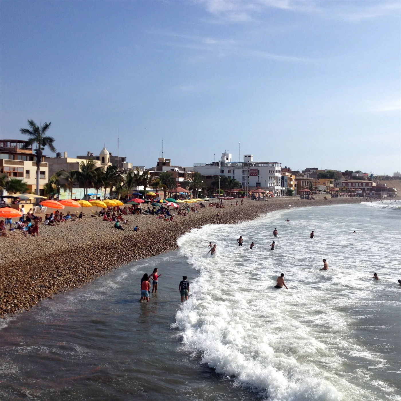 The town beach of Pacasmayo full of swimmers and umbrellas on a summer day, with the town behind