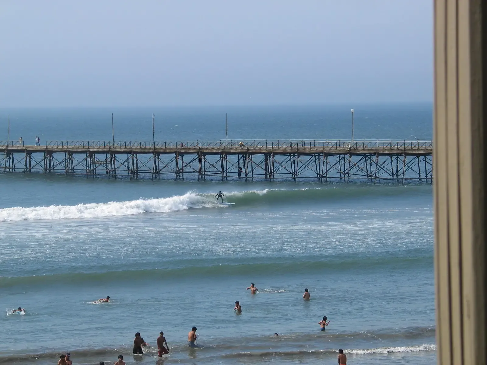 Surfer on the seafront wave, with the wooden pier behind