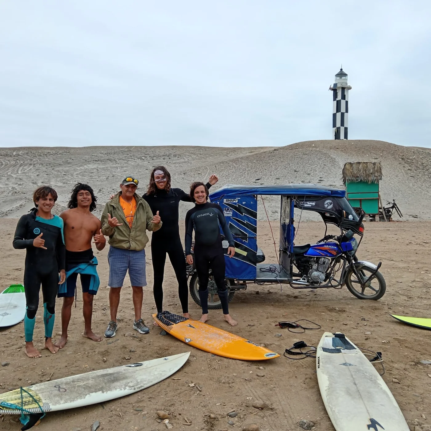 Grupo de surfistas con sus tablas junto al mototaxi, bajo el faro